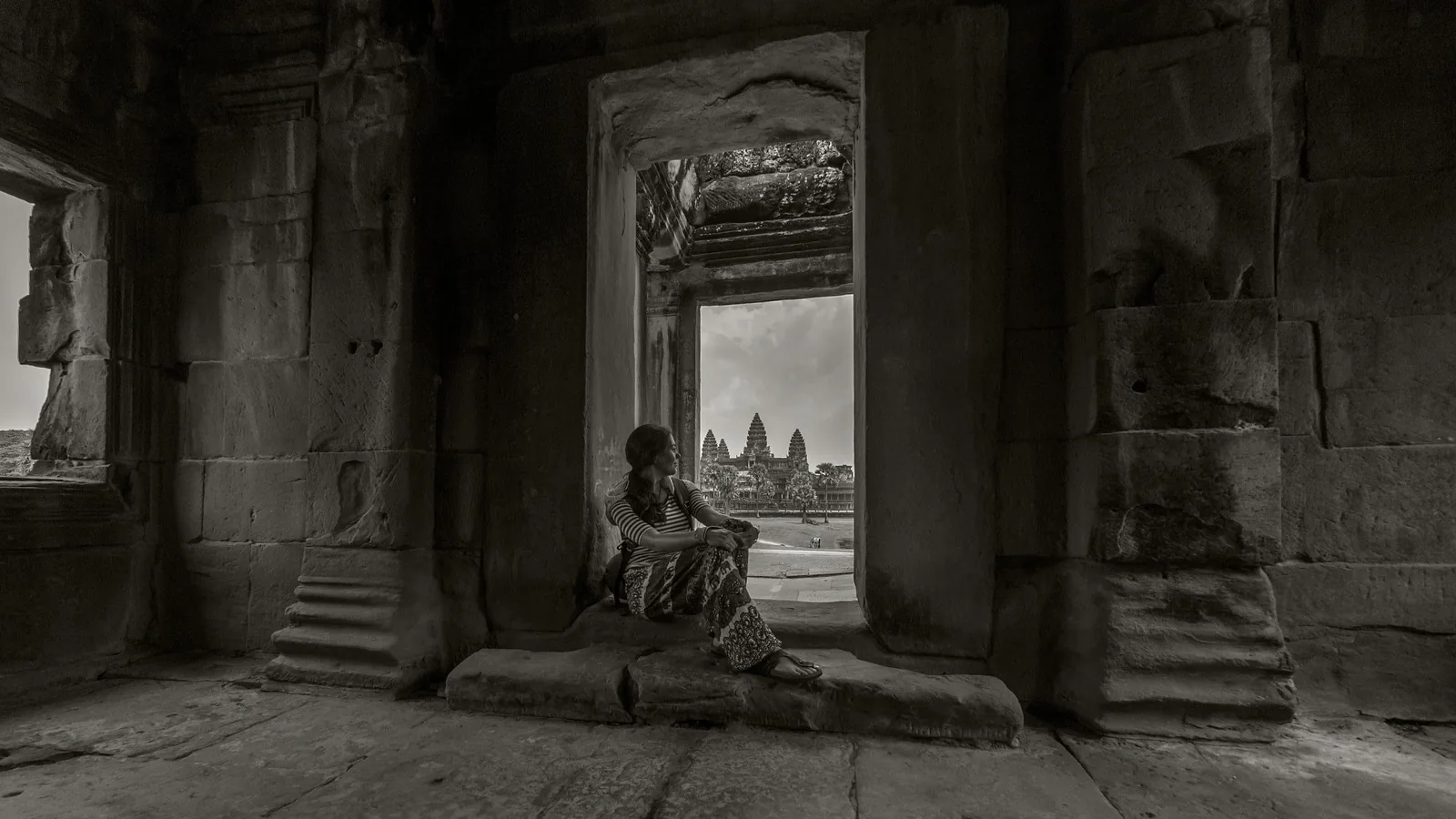 A woman sits in a stone window frame overlooking the towers of Angkor Wat near Siem Reap in this black-and-white photo. A woman sits in a stone window frame overlooking the towers of Angkor Wat near Siem Reap in this black-and-white photo.